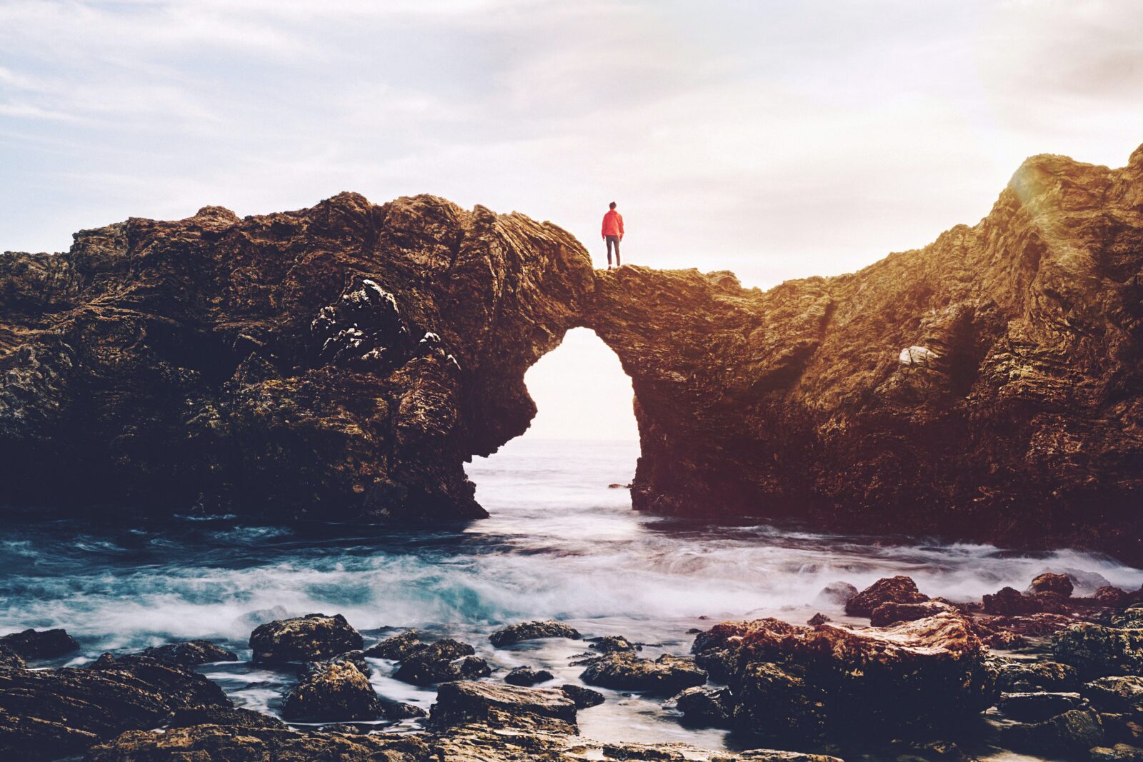Person standing on top of a rock arch above the ocean