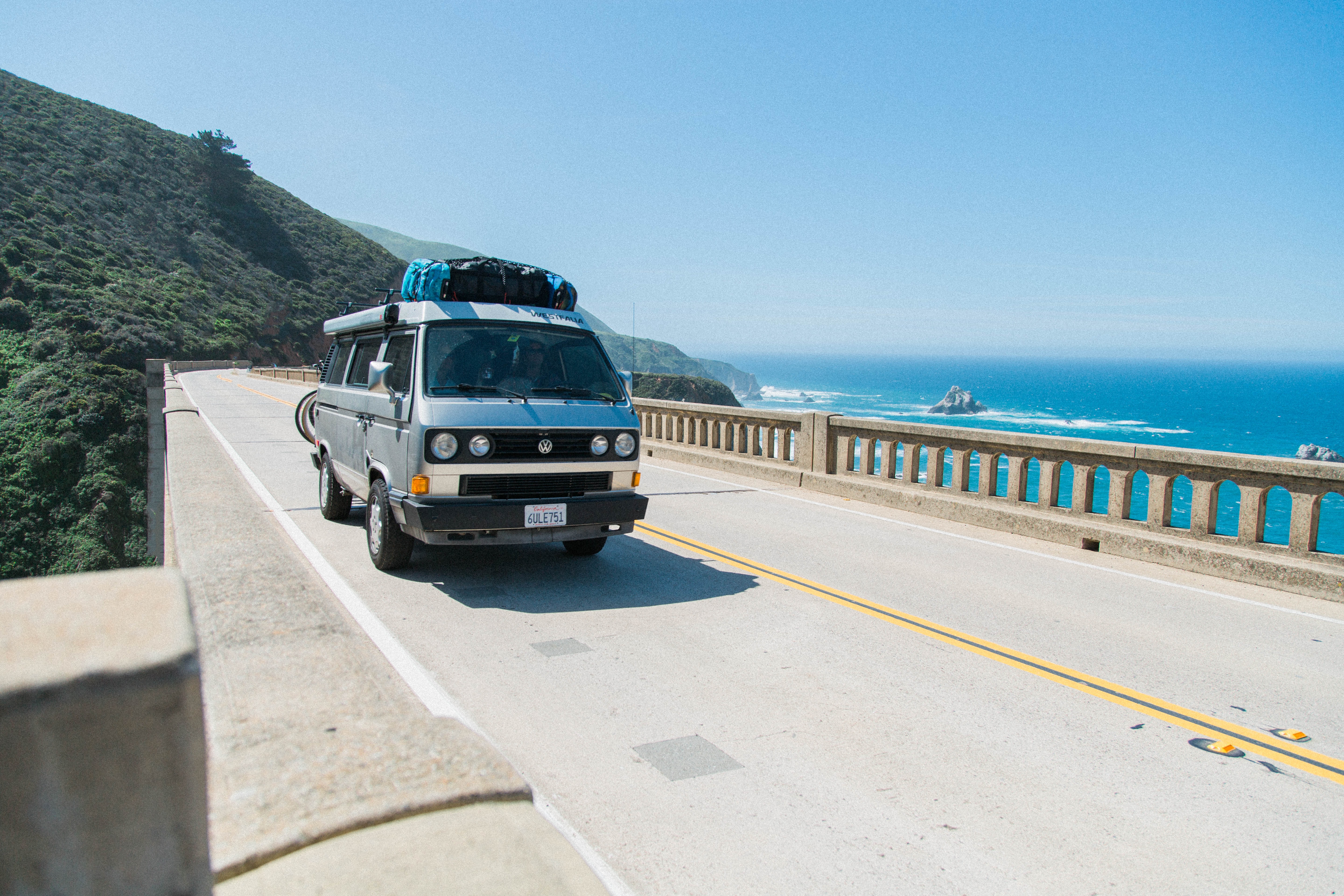 Van crossing a bridge over the ocean with hills and cliffs in the background