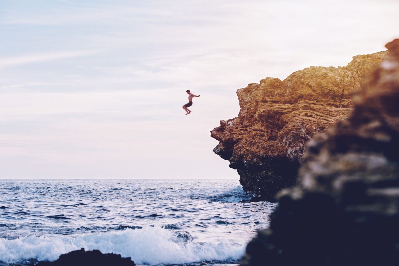 Person jumping off a rock cliff into the ocean