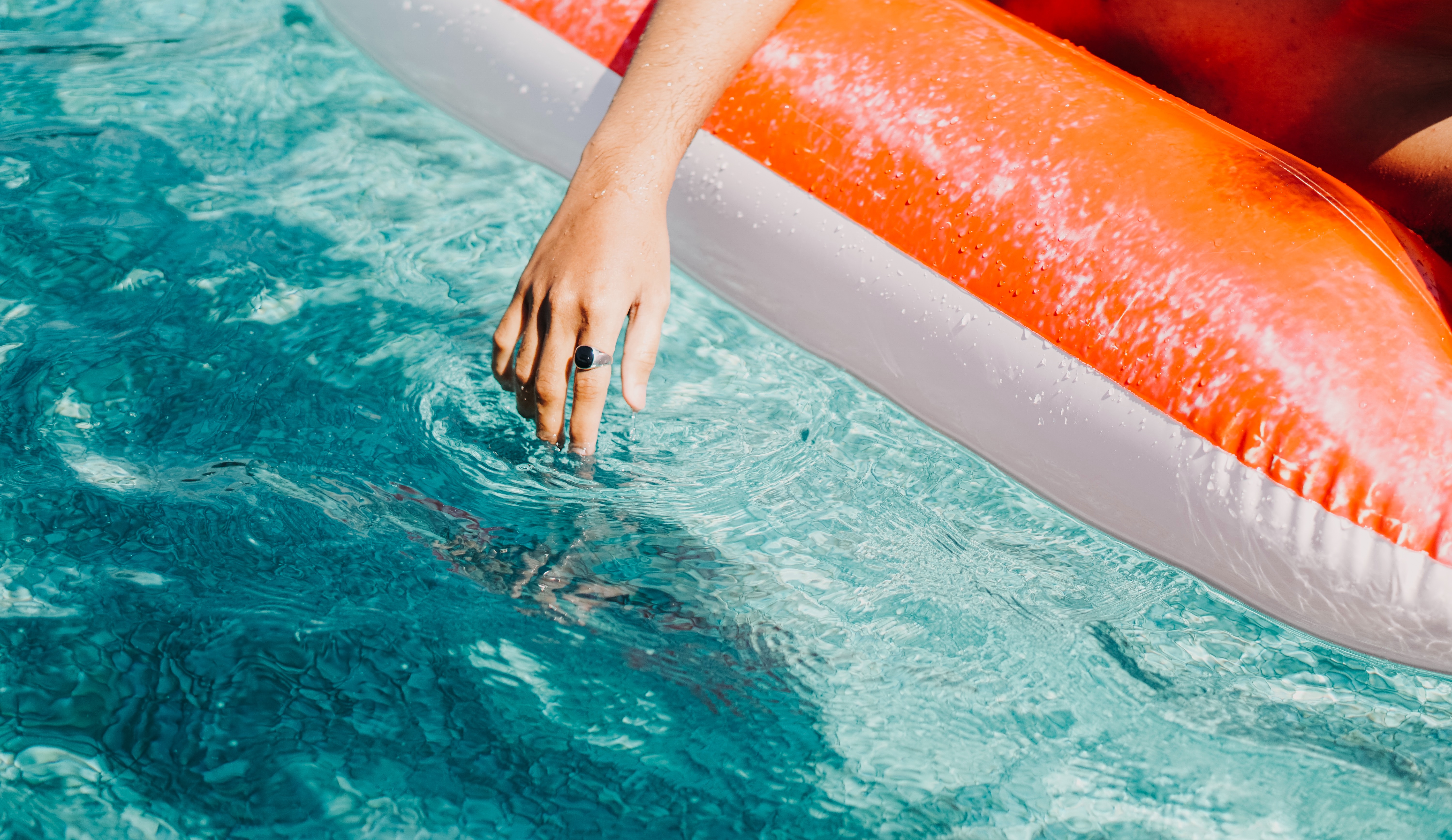 An individual peacefully floats in a pool, reclining on an inflatable raft, their hand gently caressing the water's surface