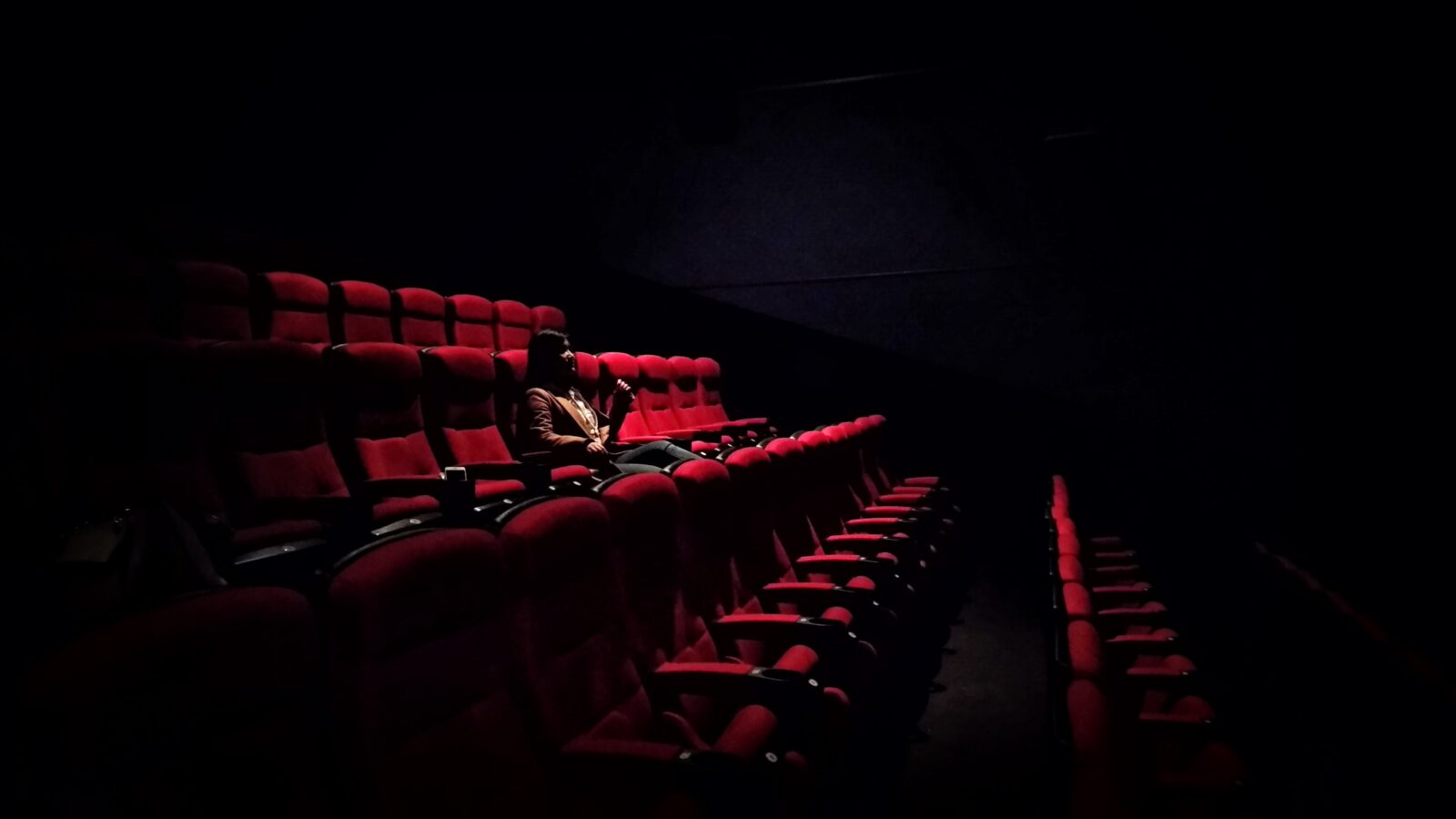 A woman reclines on a vivid red folding armchair in a movie theater.