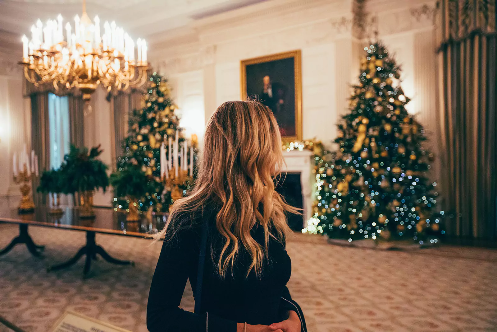 Woman in Luxury Home Wearing Long Sleeved Black Dress Viewing The Decorated Christmas Trees