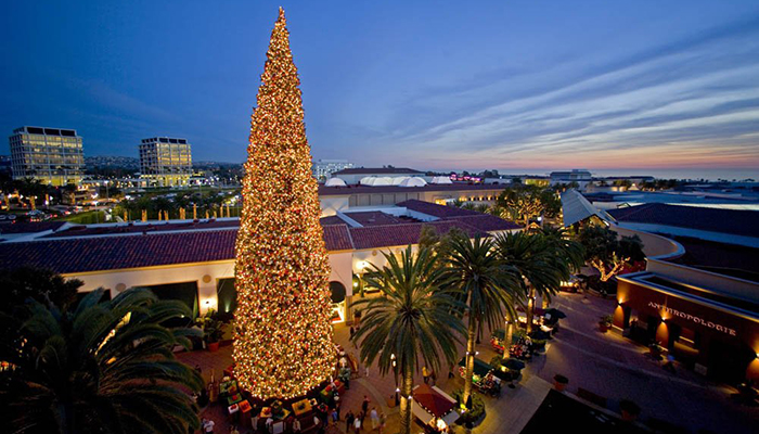 Aerial Skyline View of Fashion Island Mall at night With Large Christmas Tree full of White Lights, Large Presents, Tall Palm Trees and the store Anthropologie in the background