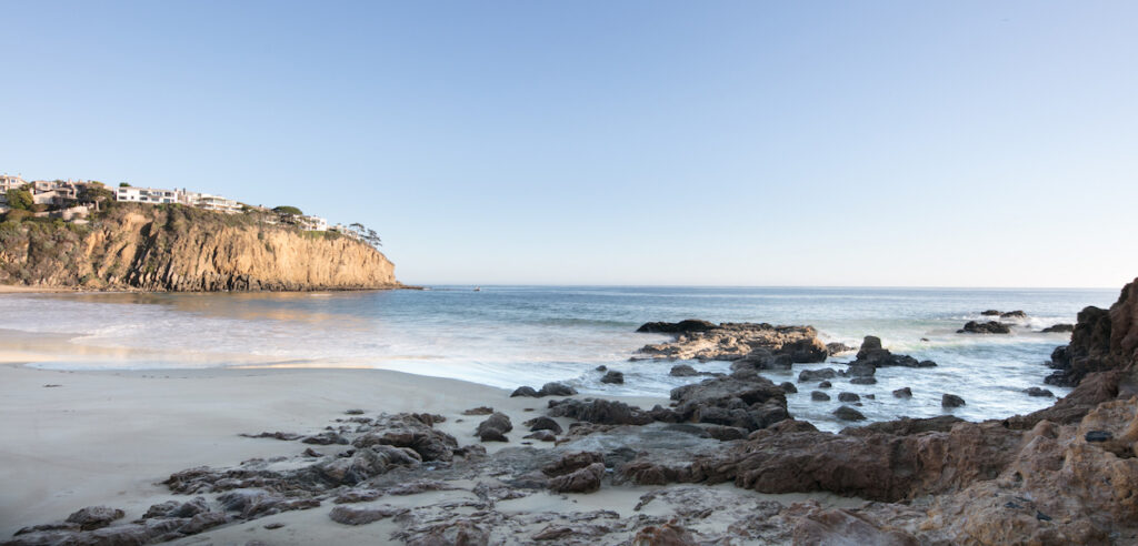 View from the beach up to the majestic bluffs where luxury homes nestle in Coastal Orange County, with the vast Pacific Ocean extending into the horizon, capturing the essence of Newport Beach, Laguna Beach, and Corona del Mar's exclusive real estate.