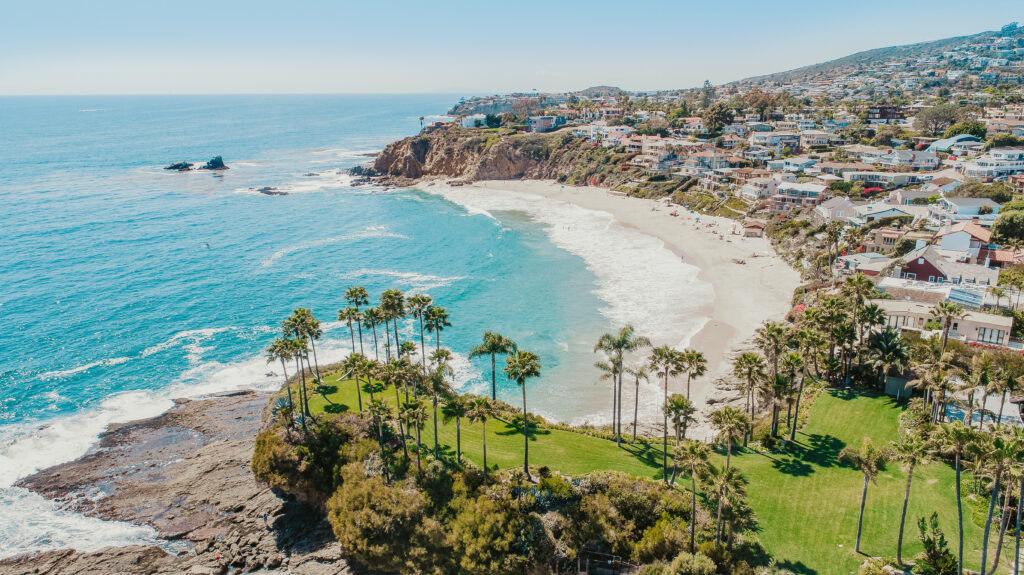 Aerial drone photo showcasing Laguna Beach luxury homes, sandy beaches, coastal bluffs, and the Pacific Ocean