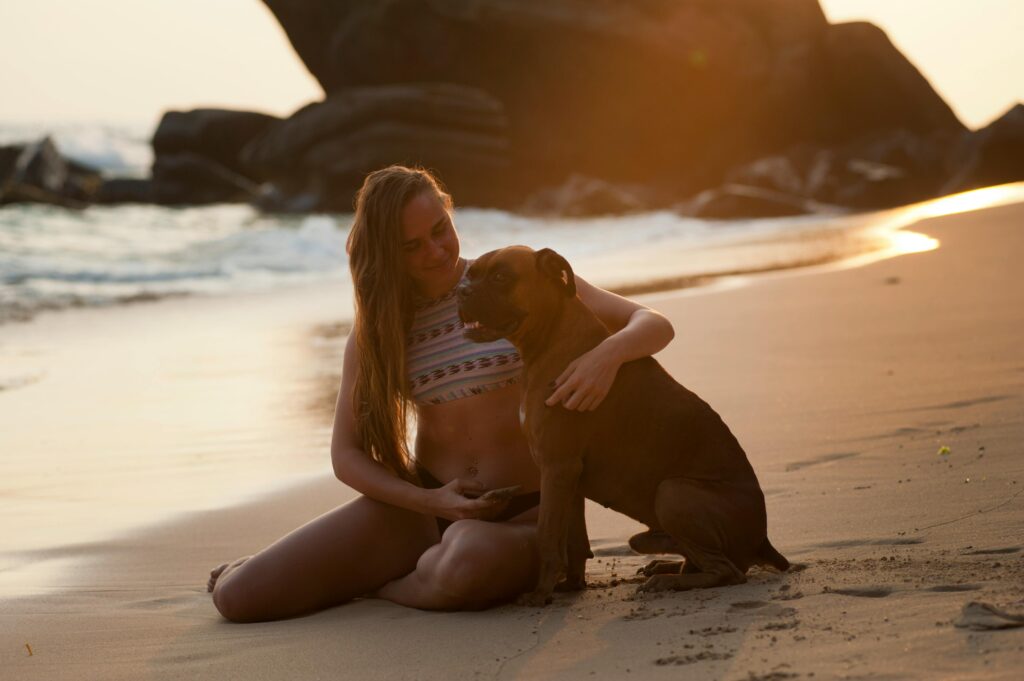Woman embraces a boxer dog on the beach shore