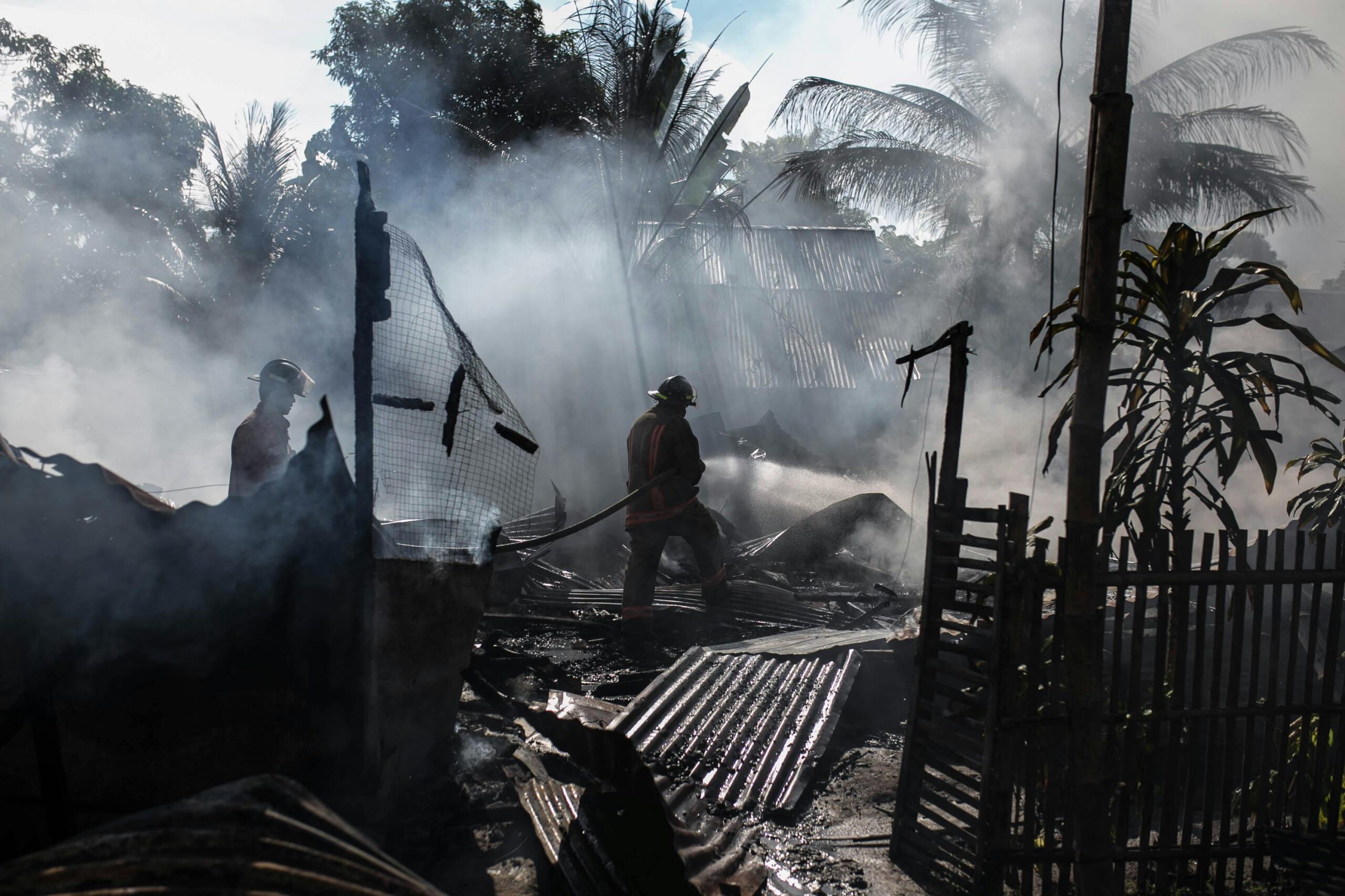 Silhouette of a firefighter holding a hose in a burned down building after a wildfire