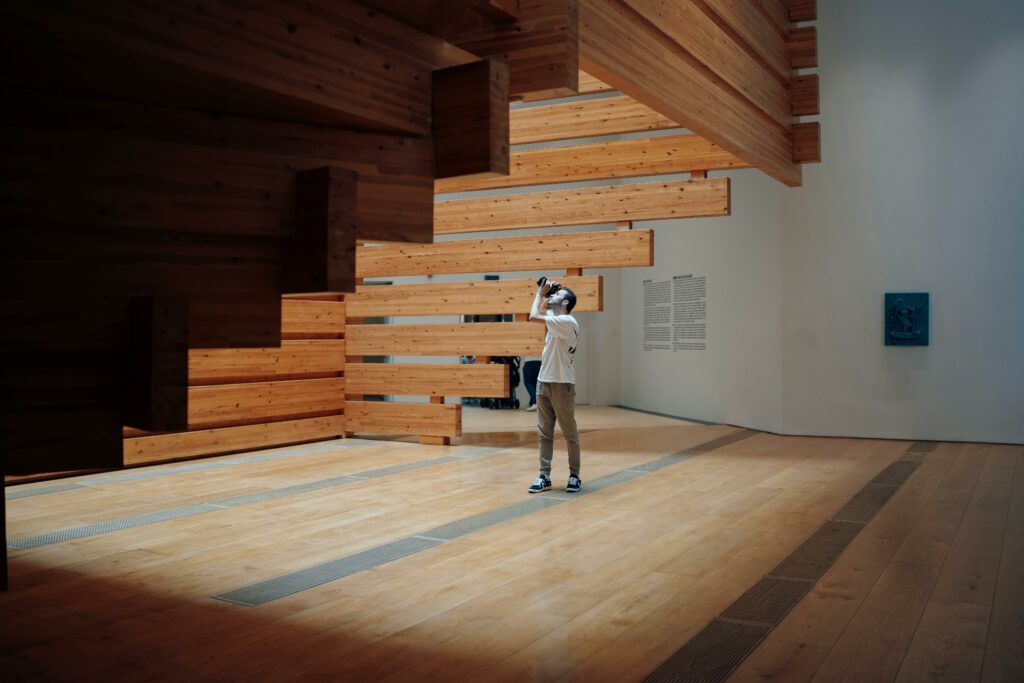 Man photographing a large wooden art installation inside an Orange County art gallery, highlighting the diverse range of fine art mediums that draw art collectors and luxury homebuyers to the area.