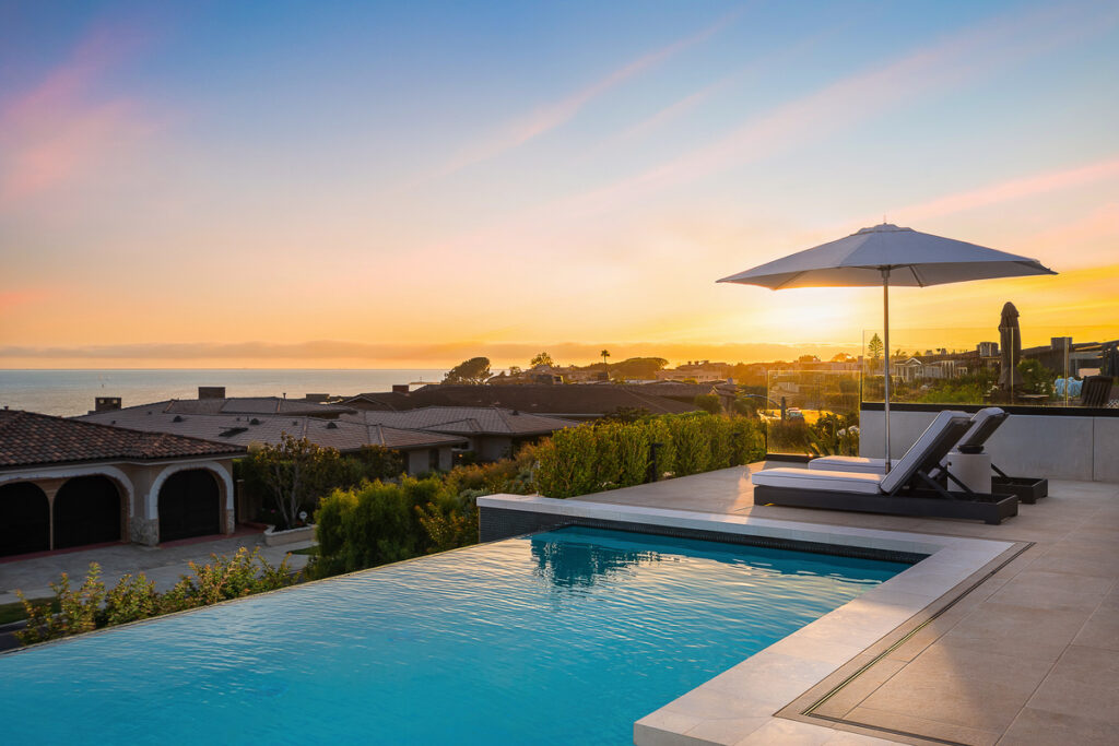 Another angle of the infinity pool at sunset, showcasing panoramic ocean views from a luxury listing sold by Andy Stavros and his team in Corona Del Mar. The tranquil setting highlights the premium coastal lifestyle offered by homes in this exclusive Orange County enclave. The pool reflects the vibrant colors of the sunset, creating a serene and picturesque atmosphere.