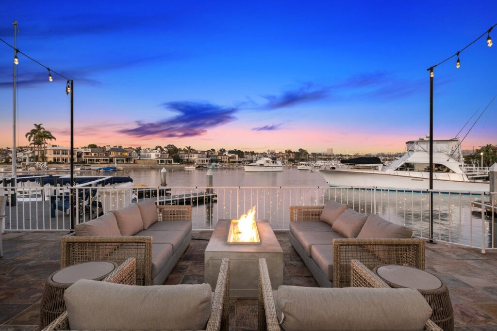 Outdoor patio with fire pit overlooking boats in Newport Harbor at a bayfront luxury home for sale by the best realtors Andy Stavros Group