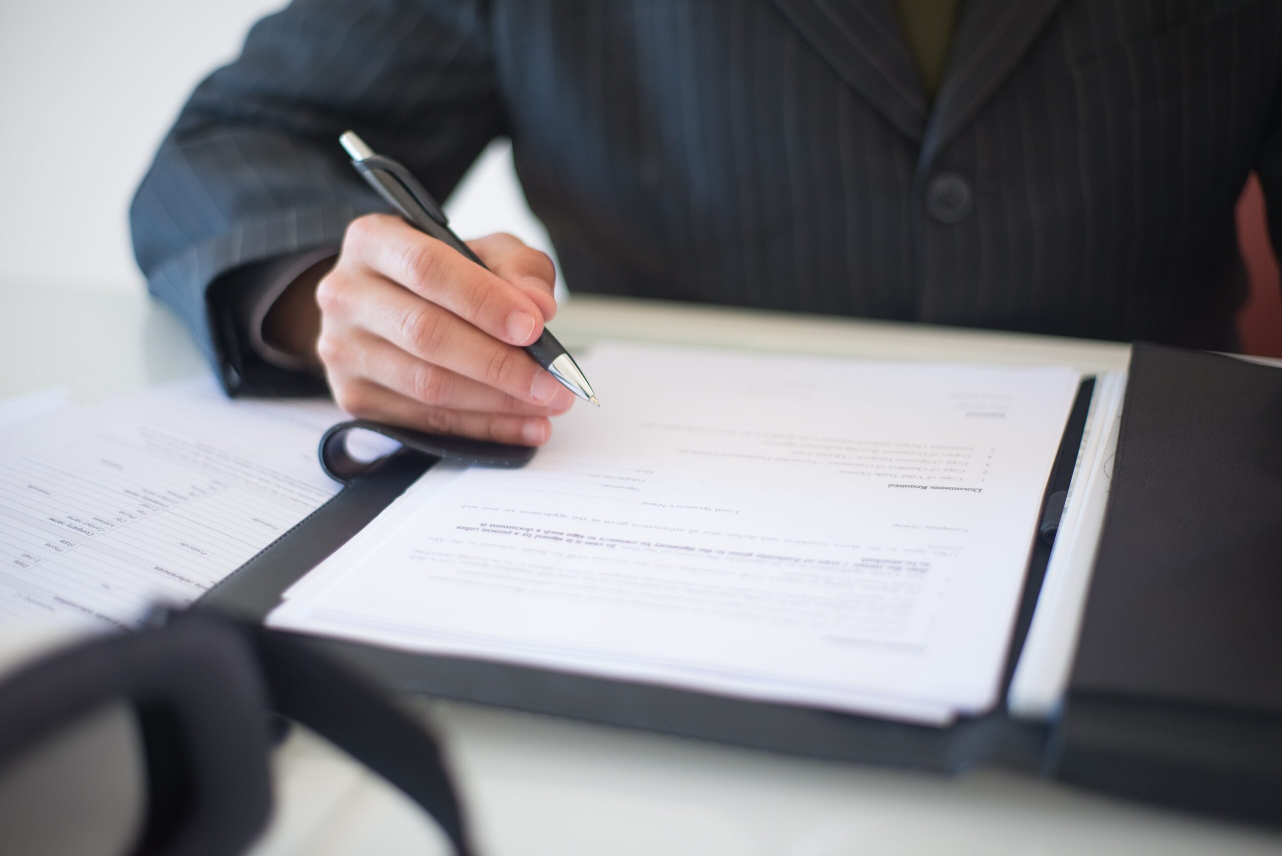 Person’s hands holding a pen and paper signing a contract, representing buying real estate in a trust in California for your Orange County home